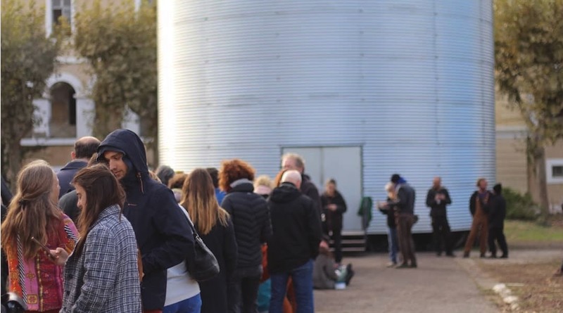 A group of people gathering outside a cylinder-shaped building