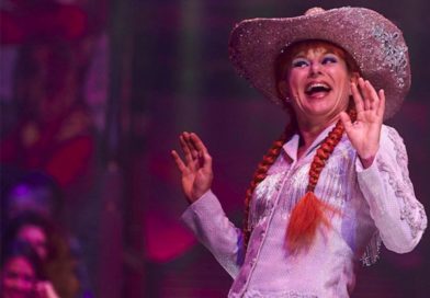 Petra Massey smiles before the crowd, wearing her red hair in long pigtail braids and a cowboy hat