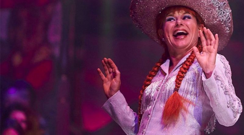 Petra Massey smiles before the crowd, wearing her red hair in long pigtail braids and a cowboy hat