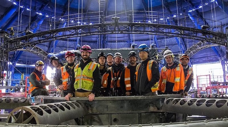 A group of riggers stand together wearing yellow and orange vests