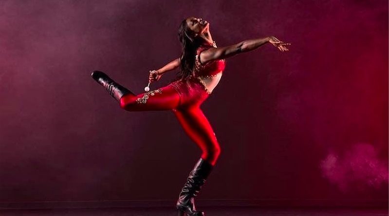 Sarah Louis-Jean wears a red jumper and stand in an attitude position, with her arm outstretched