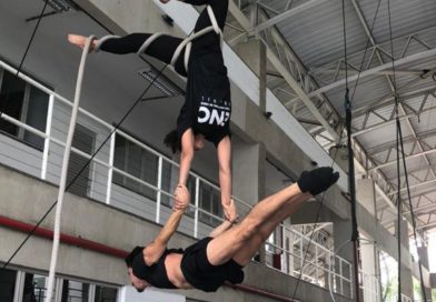 An aerialist hangs from a web holding a flyer in a lever