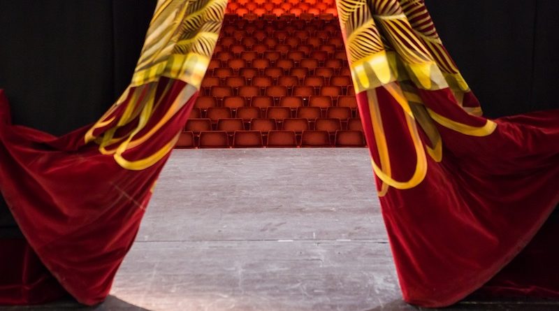 A backstage photo shows an arena from behind red curtains