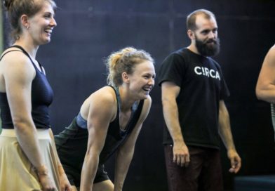 Rowan Hayden-White, profile, leans her hands on her knees and smiles. Next to her is a person with a beard wearing a black Circa tshirt.