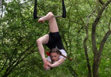 Aerialist pulls her leg over her head hanging from a static trapeze