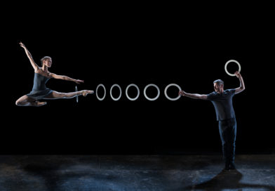 a dancer jumps with a leg extended to the right of the image, a juggling ring is suspended around her ankle a series of juggling rings extend to a circus juggler's hand