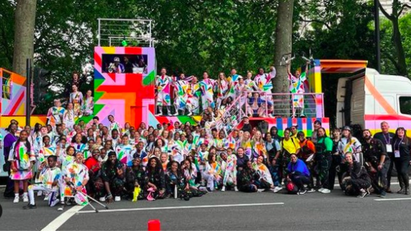 The Steppaz pose along Cirque Bijou performers at the Queen's Platinum Jubilee Pageant. The group stands on a colorful parade float with a Union Jack design