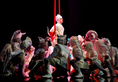 Cirque du Soleil artists in costume for ECHO. The Cartographer, on aerial straps, sits loosely above performers dressed as paper animals.